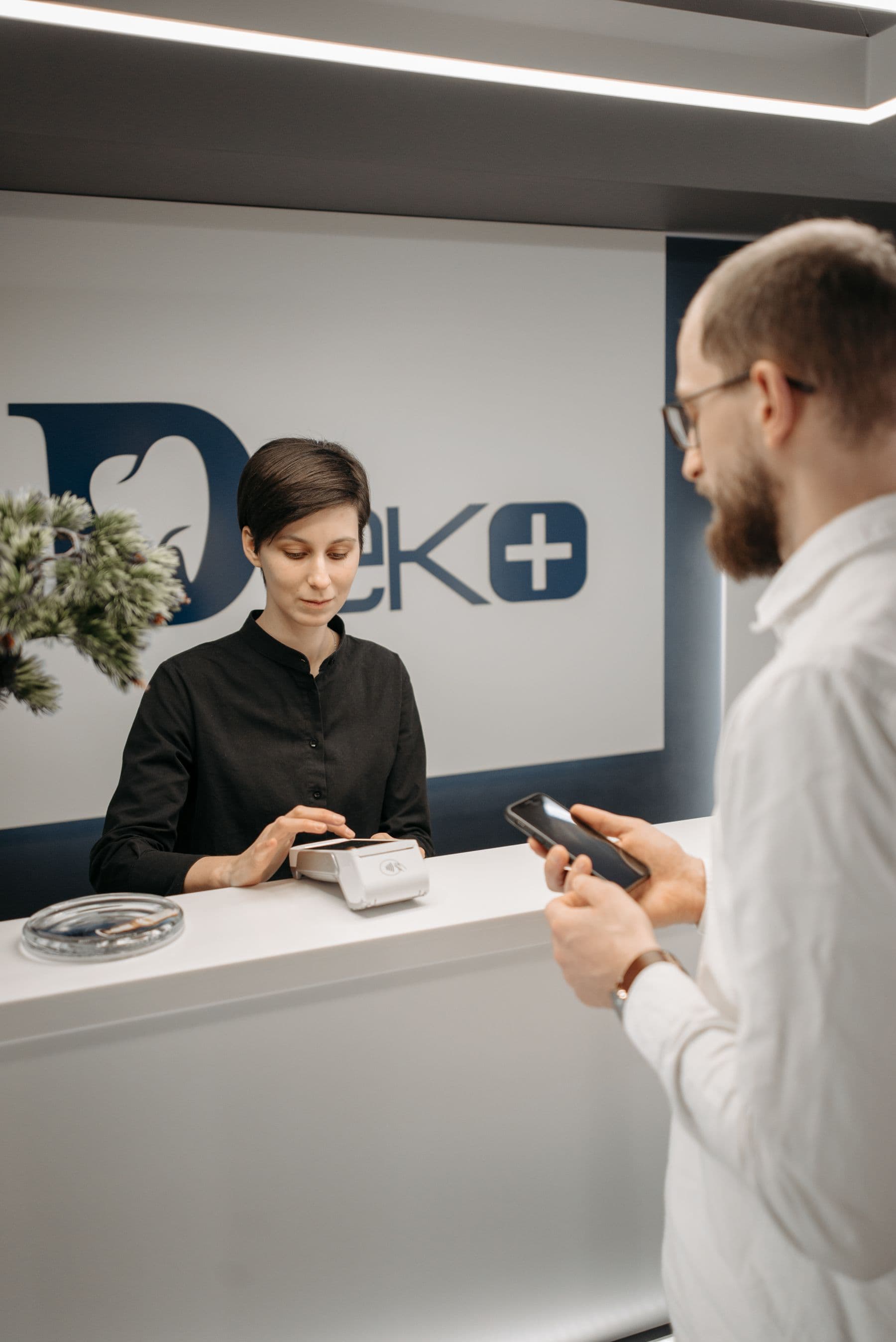 A patient paying at a clinic reception desk with a phone and card terminal